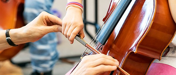 En person får hjälp med hur man håller stråken när man spelar cello.